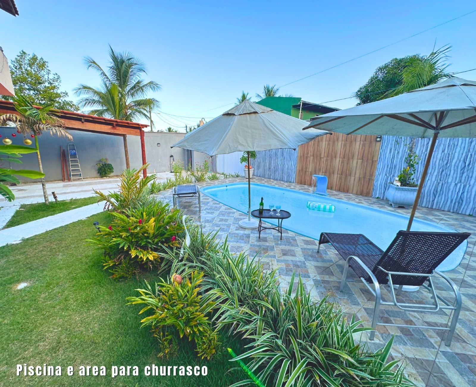 Piscina e área para churrasco cercadas por jardim
